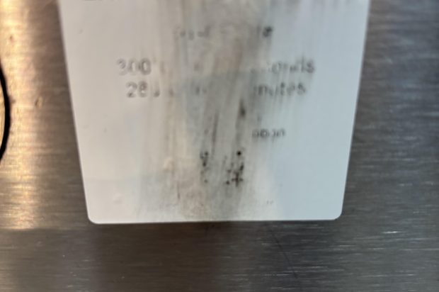 A smudged and partially illegible product label from Expert Labels Ltd., affixed to a metallic surface, showing faded print and black streak marks.