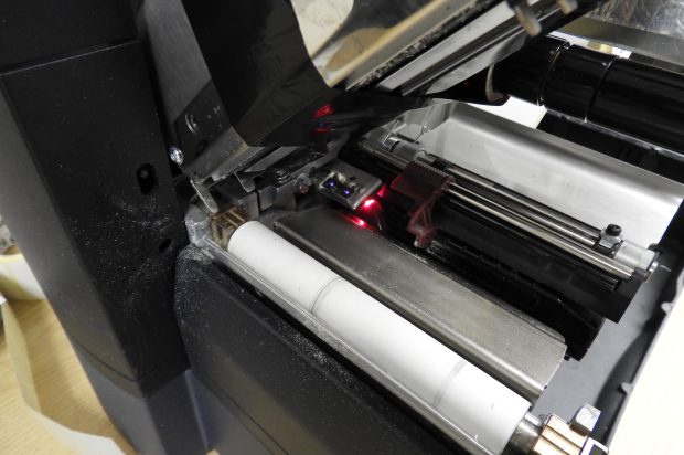 Close-up of the inside of a thermal label printer showing visible dust build-up on the rollers and components, highlighting the need for routine cleaning and maintenance.